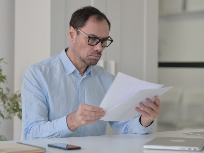 A man in glasses reads documents in his office, a taxpayer reading about tax debt loans to deal with tax debt