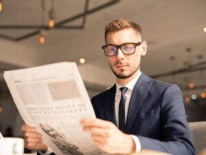 A man in a suit and glasses reads the newspaper