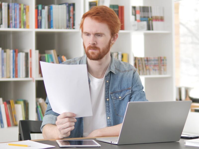 A man with red hair reads a document, an investor reading his interest payments so he can claim deductions with the ATO