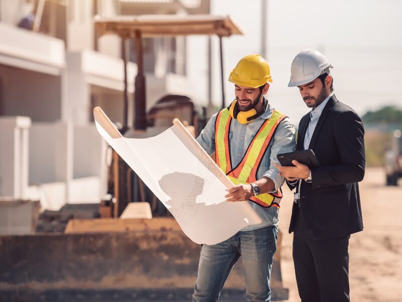 Civil construction worker and developer happily discuss construction plans, equipment and ongoing construction project in the background