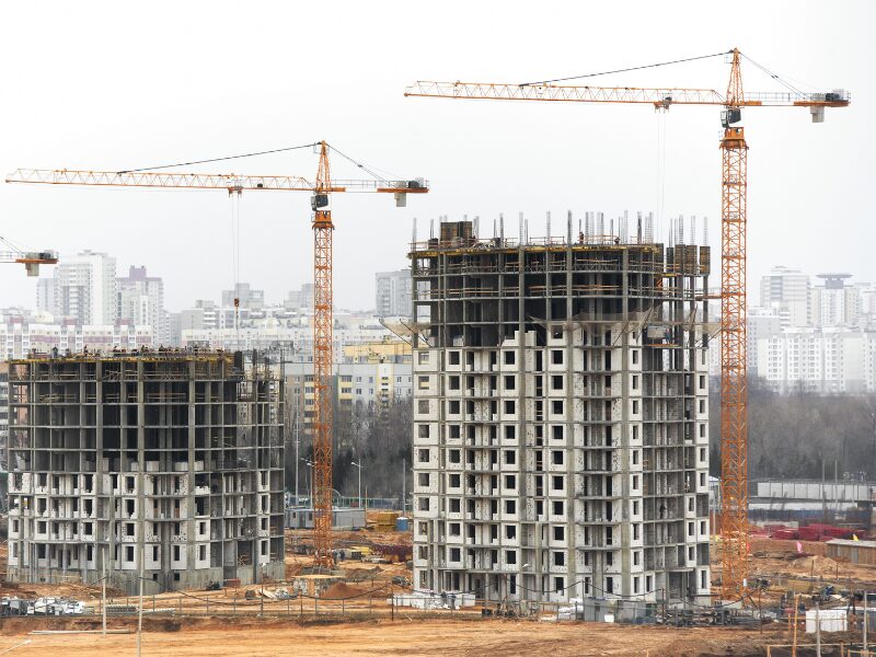 Two commercial buildings under construction, large cranes working on the buildings