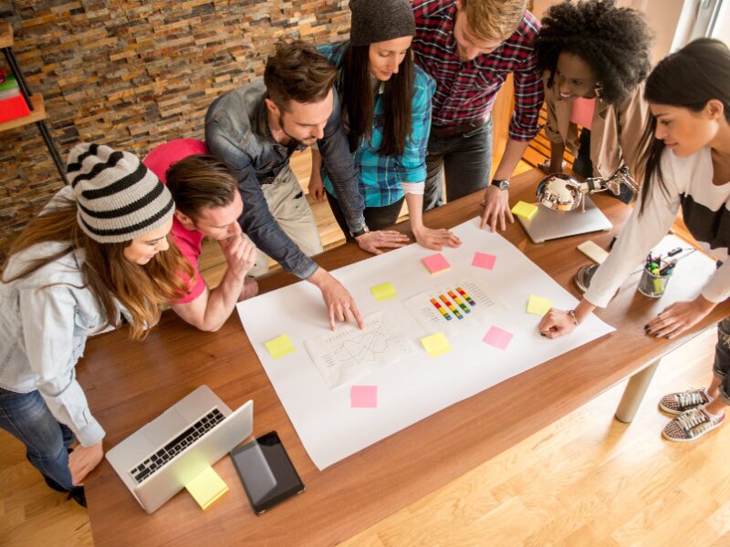A large group of people working at a startup gathered at a table discussing plans for financing and the business’s future