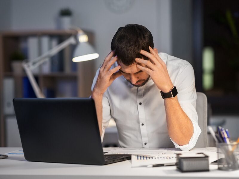 Man holding his head in his hands, looking down as he reads documents, man looking at his rejected home loan application