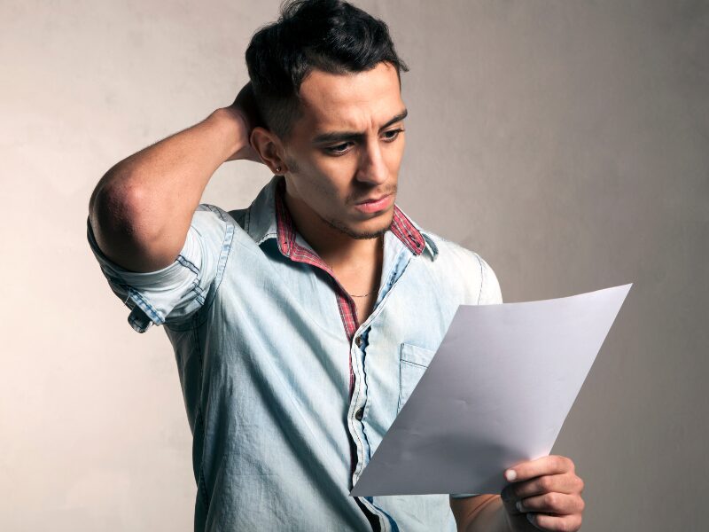 Man with his hand behind his head, stressed while reading a document, Self-employed applicant reviewing his rejected home loan application