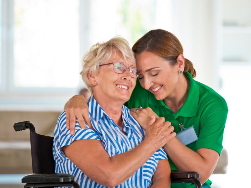 NDIS worker warmly embraces elderly patient in a wheelchair