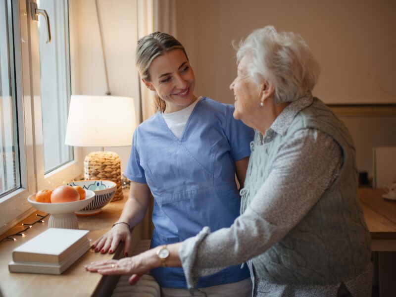 NDIS worker talks to elderly patient as they stand by the window