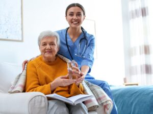 NDIS worker assists an elderly woman with holding a glass of water, looking at the camera and smiling