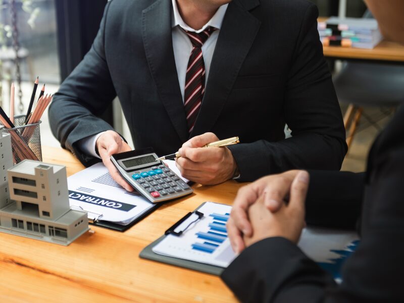 Cropped photo of a mortgage broker pointing to a calculator with a pen, presenting to a client, savings after refinancing