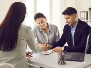 A business-owning couple meet with a mortgage broker or lender to sign a refinancing loan agreement