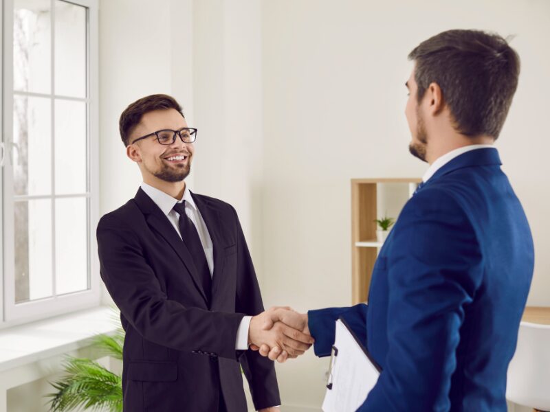 Two men in suits happily shake hands, a mortgage broker and business owner finalise a refinancing solution
