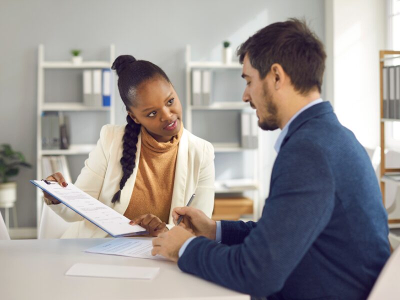 A mortgage broker discusses a document with a business owner, pointing at where he should sign