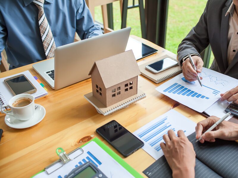 Cropped photo of a home loan meeting between broker and client, cardboard model house in the middle of the table