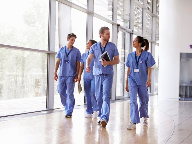 A group of allied health professionals walk through a hallway with large windows