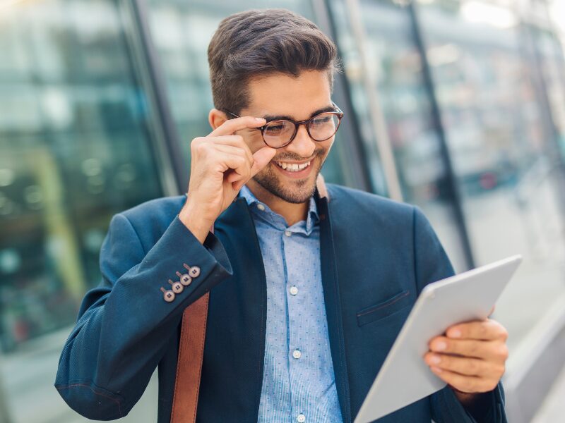 Happy businessman adjusts his glasses as he reads the screen of an electronic tablet