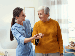 An NDIS provider happily holds the hand of an elderly patient as she assists her with walking