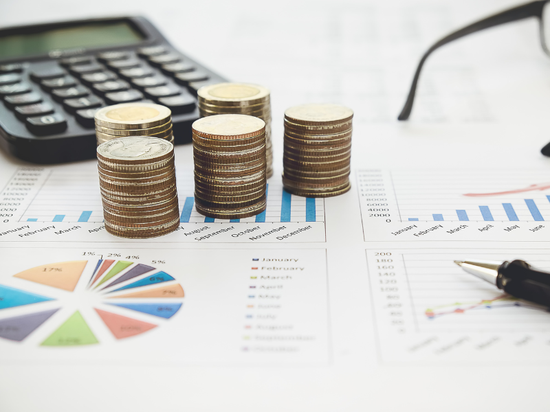 Several piles of coins, a calculator, glasses, and a pen placed on top of a document