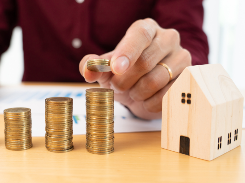 A man stacking coins next to a miniature wooden house
