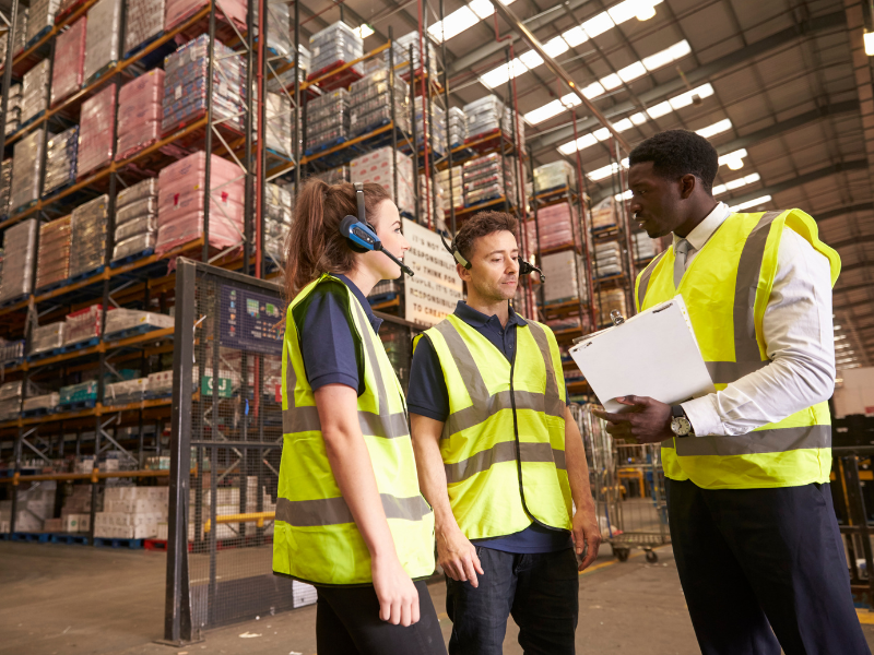 Workers of a supplier company talking, three workers in high visibility vests having a discussion inside a supplier warehouse