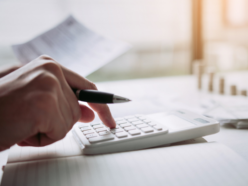 A hand holding a pen using a white calculator
