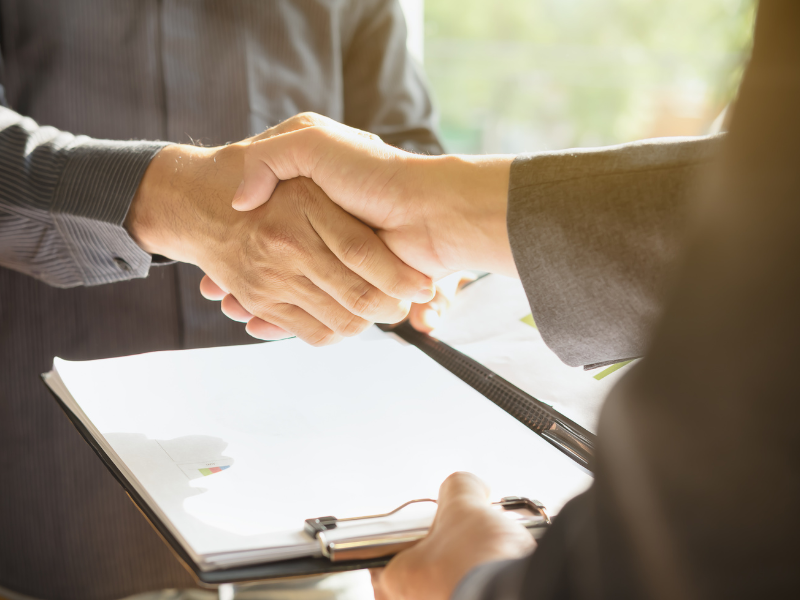 Cropped photo of two people shaking hands while holding a clipboard with documents