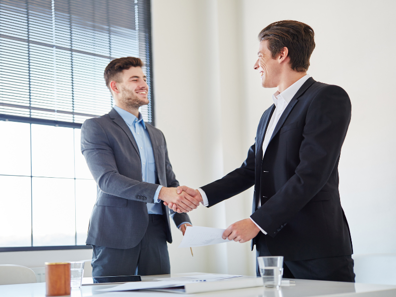 Two men in suits in a professional setting shake hands happily, mortgage broker or lender and a business owner agree on loan terms