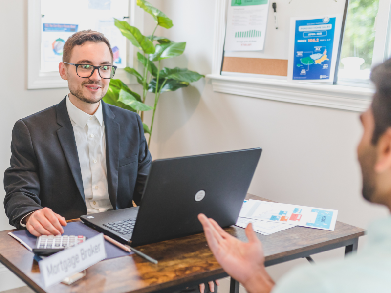 A mortgage broker with a laptop on his desk happily meets a client