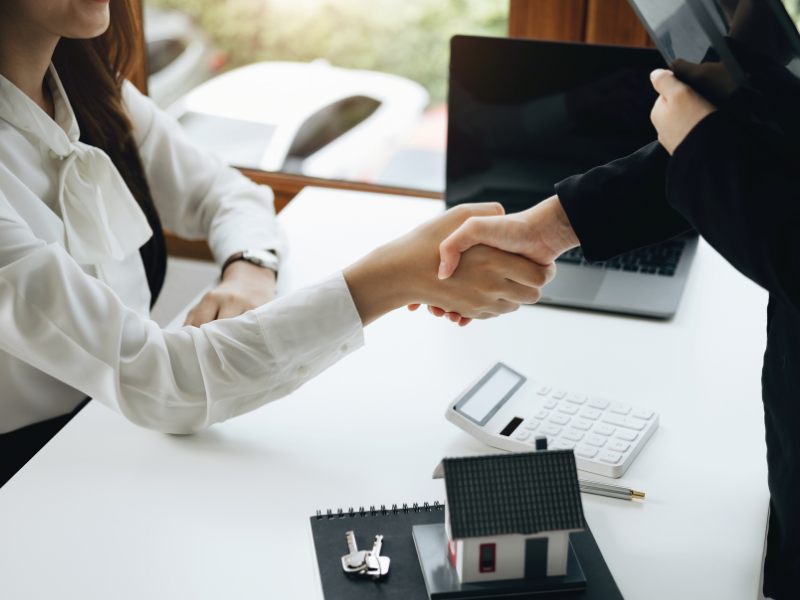 A mortgage broker on her feet shakes the hand of a client who is sitting down