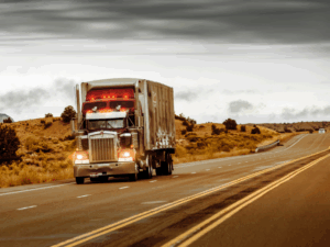A red and stainless steel large freight truck driving down the road on an overcast day