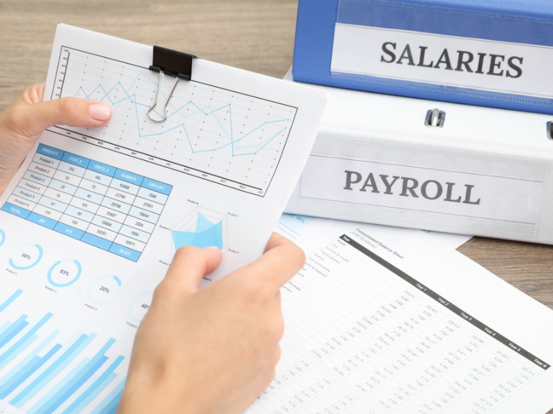 Hands holding documents, large folders labeled salaries and payroll in the background