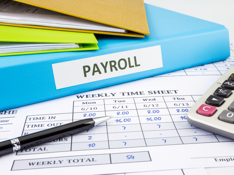 An employee’s timesheet, a folder labelled ‘payroll’ on top of it, a pen and calculator visible