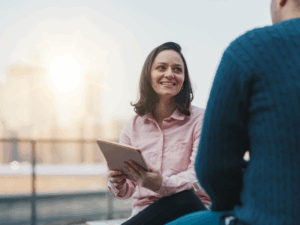 A mortgage broker smiles while holding an electronic tablet, discussing how a business line of credit works to a business owner