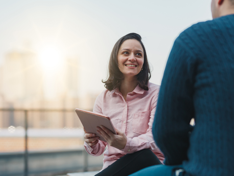 A mortgage broker smiles while holding an electronic tablet, discussing how a business line of credit works to a business owner