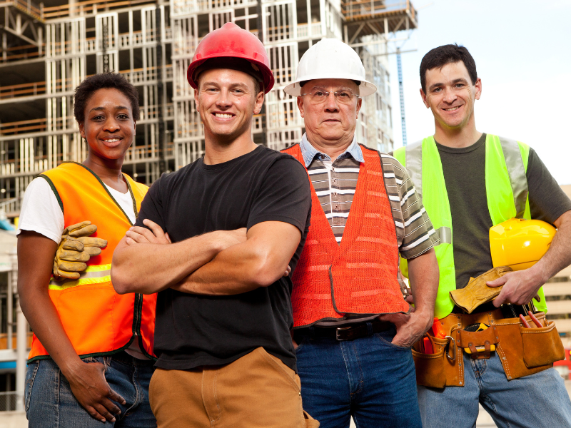 A group of diverse construction workers in safety gear poses and smiles at the camera
