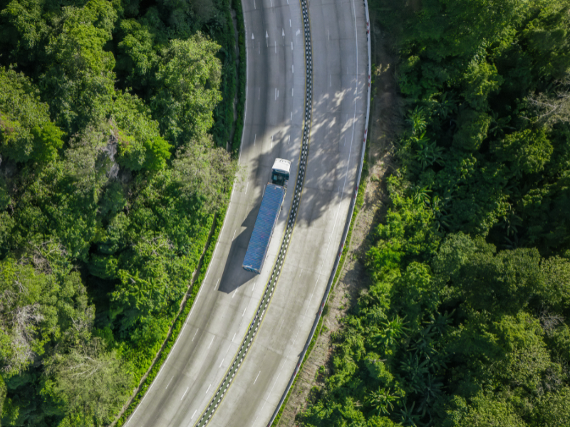 Drone shot of a large transport truck driving down a road surrounded by trees