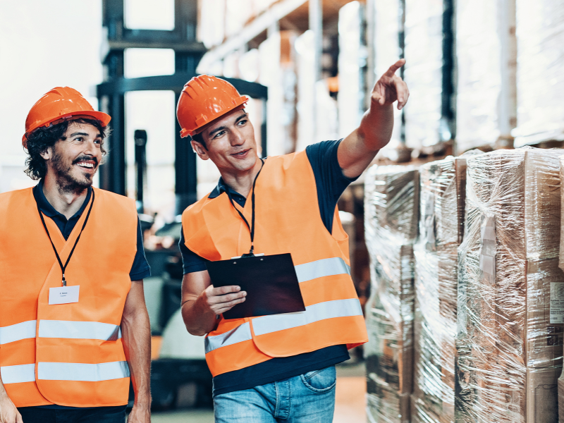 An employee at a warehouse shows boxes and shelves to a new employee