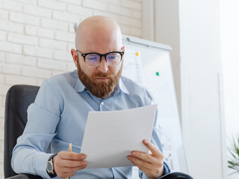 A man in glasses reads documents, reading about payment plans for unpaid super