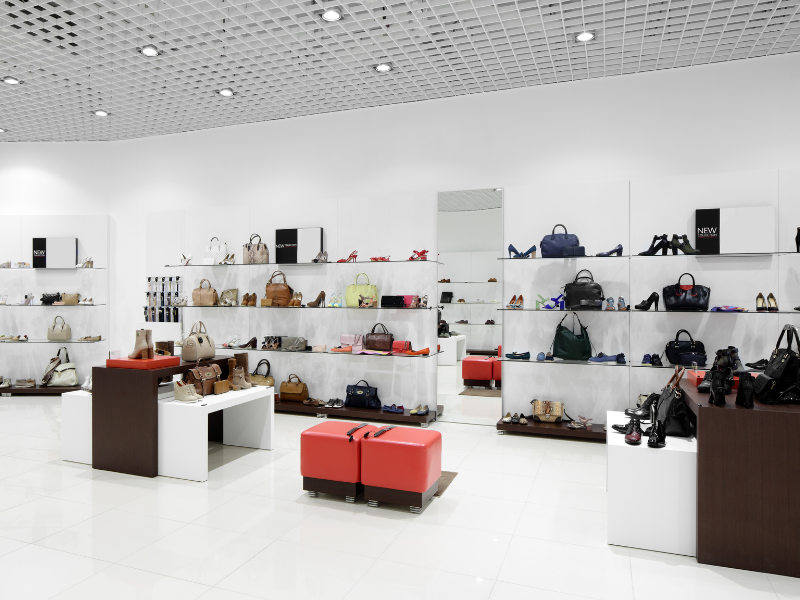 The inside of a brightly lit clean looking retail store displaying bags and shoes