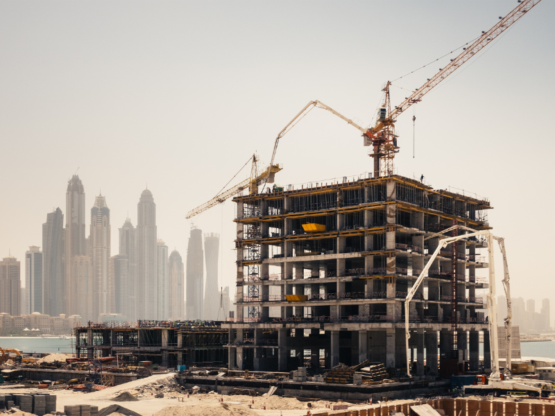 An ongoing construction project with multiple cranes working, a cityscape in the background