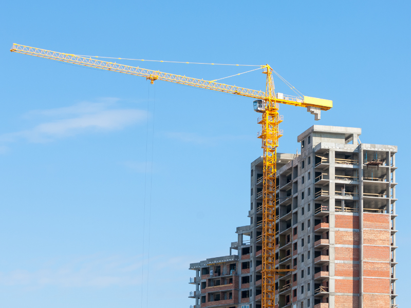 A large yellow crane and a building under construction set against the background of clear blue skies