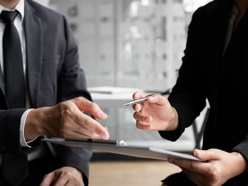 Cropped photo of two people discussing documents on a clipboard, a mortgage broker showing working capital loan details to client