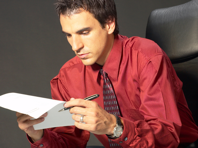 A man in a red shirt and tie intently reads a document, business owner going over his unpaid tax liabilities with the ATO