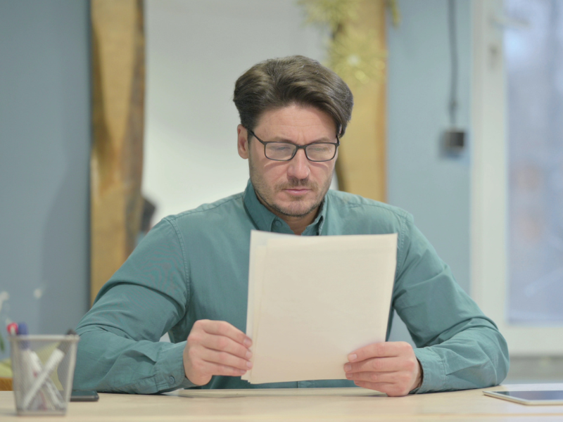 A man in glasses intently reads documents, a business director receiving a director penalty notice from the ATO