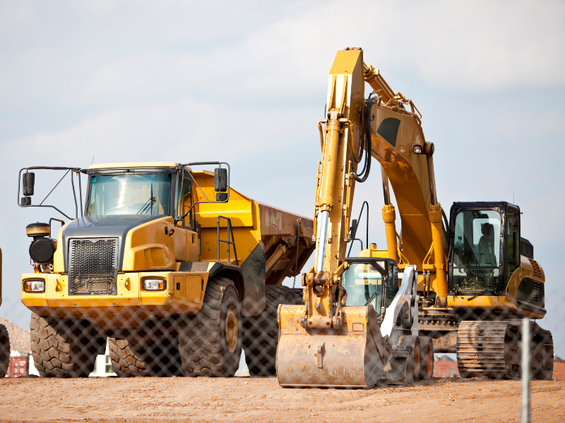 A yellow dump truck and excavator parked behind a chicken wire fence