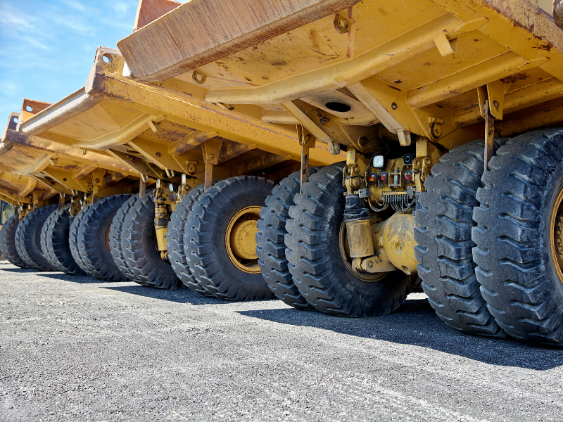 A row of parked large yellow construction equipment, parked dump trucks, zoomed in on the back wheels