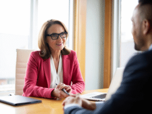 A woman in glasses cheerfully speaks with a man in a suit, a mortgage broker discusses refinancing with a business owner