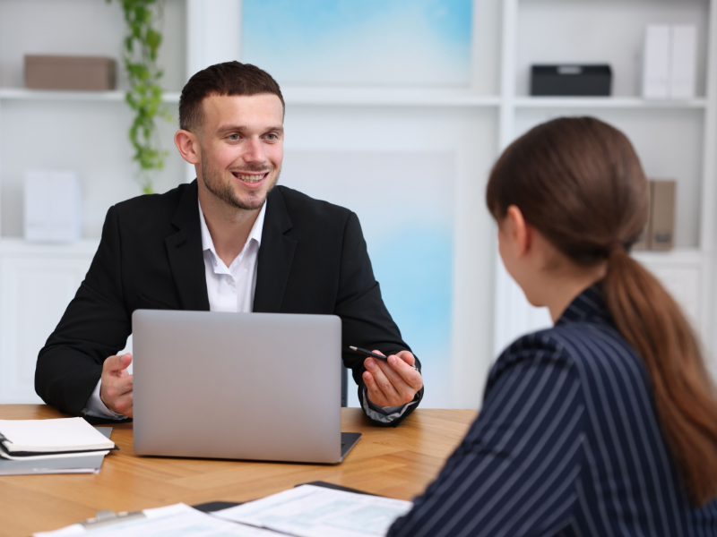 A mortgage broker with a laptop smiles as he talks to a business owner about business line of credit options