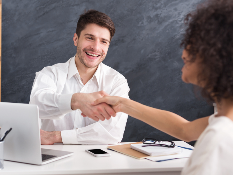 A loan broker smiles as he shakes hands with a business owner client, agreeing on a business line of credit solution