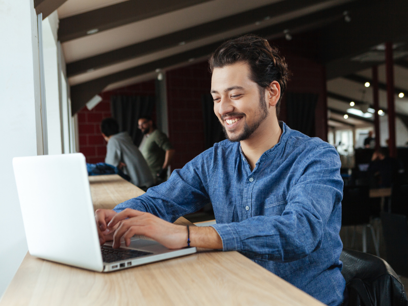 A man smiles as he uses his laptop on a counter by the window, business owner choosing the right funding solution