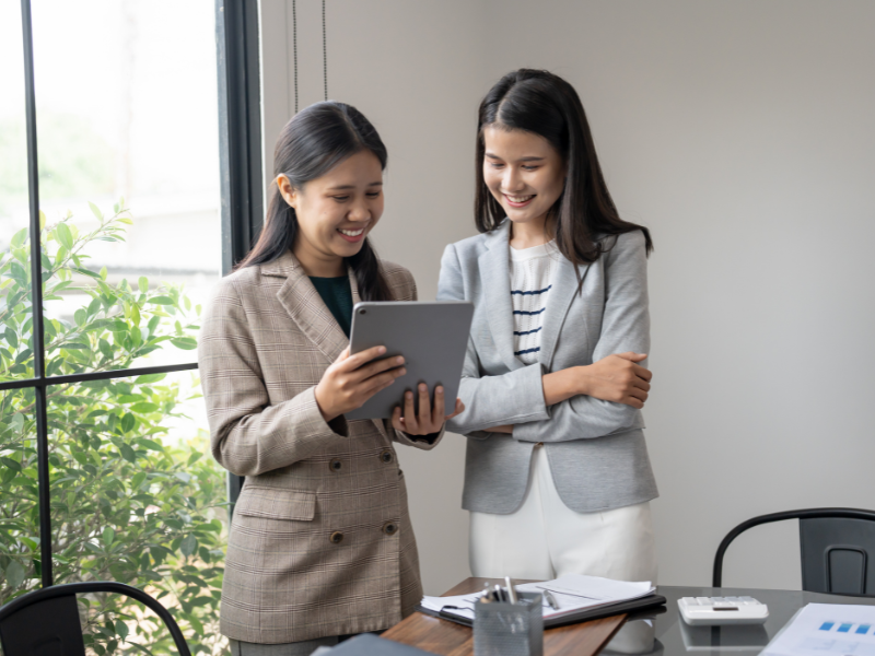 A mortgage broker happily shows loan details to a business owner through an electronic tablet
