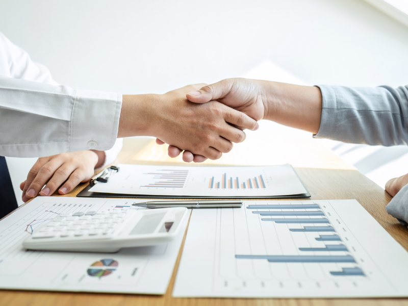 Two hands shaking, a calculator, a pen, and documents on the table, a business owner and mortgage broker agreeing on a loan solution